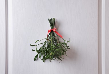 Mistletoe bunch with red bow hanging on white wooden door. Traditional Christmas decor