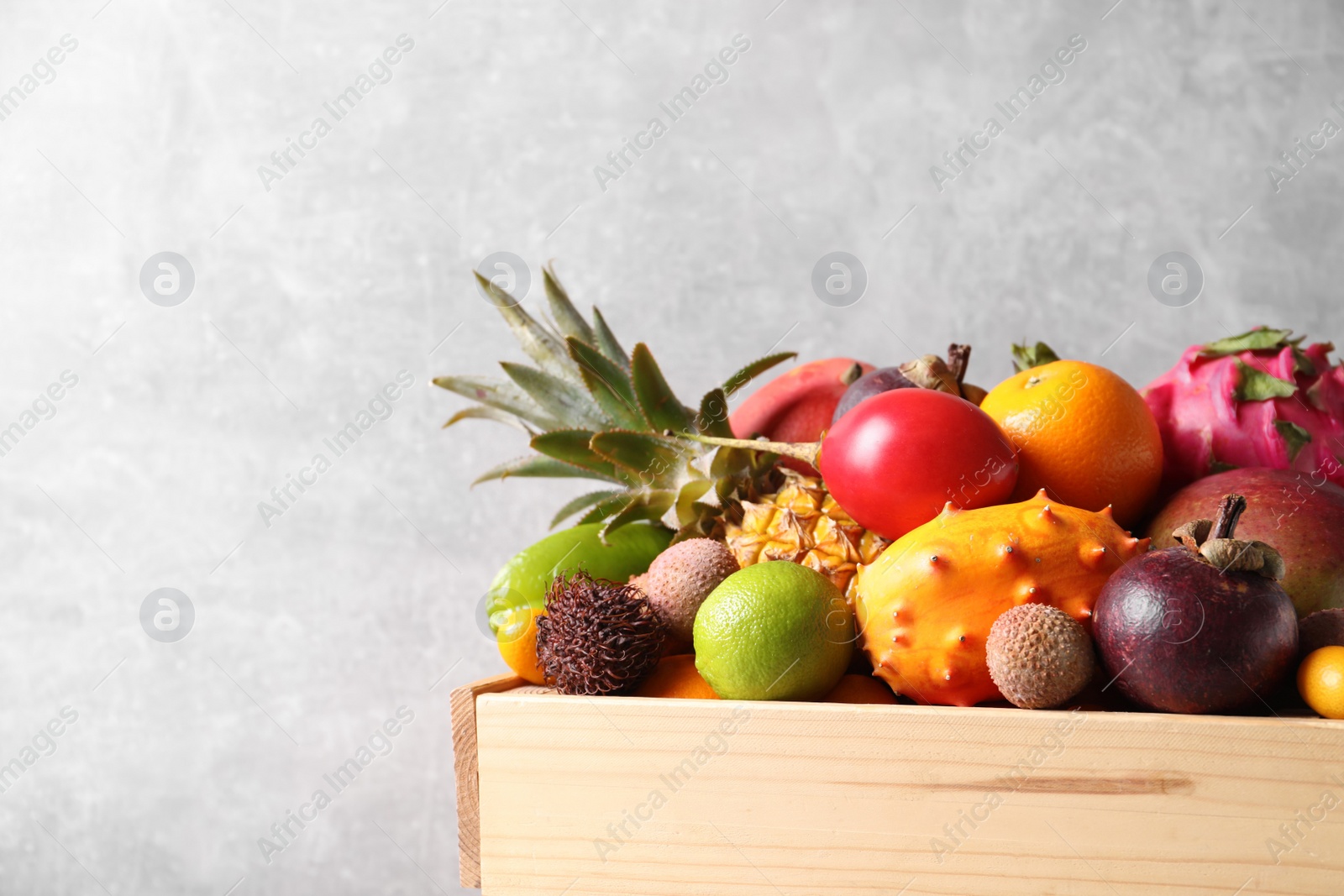 Photo of Crate with different exotic fruits on light grey background