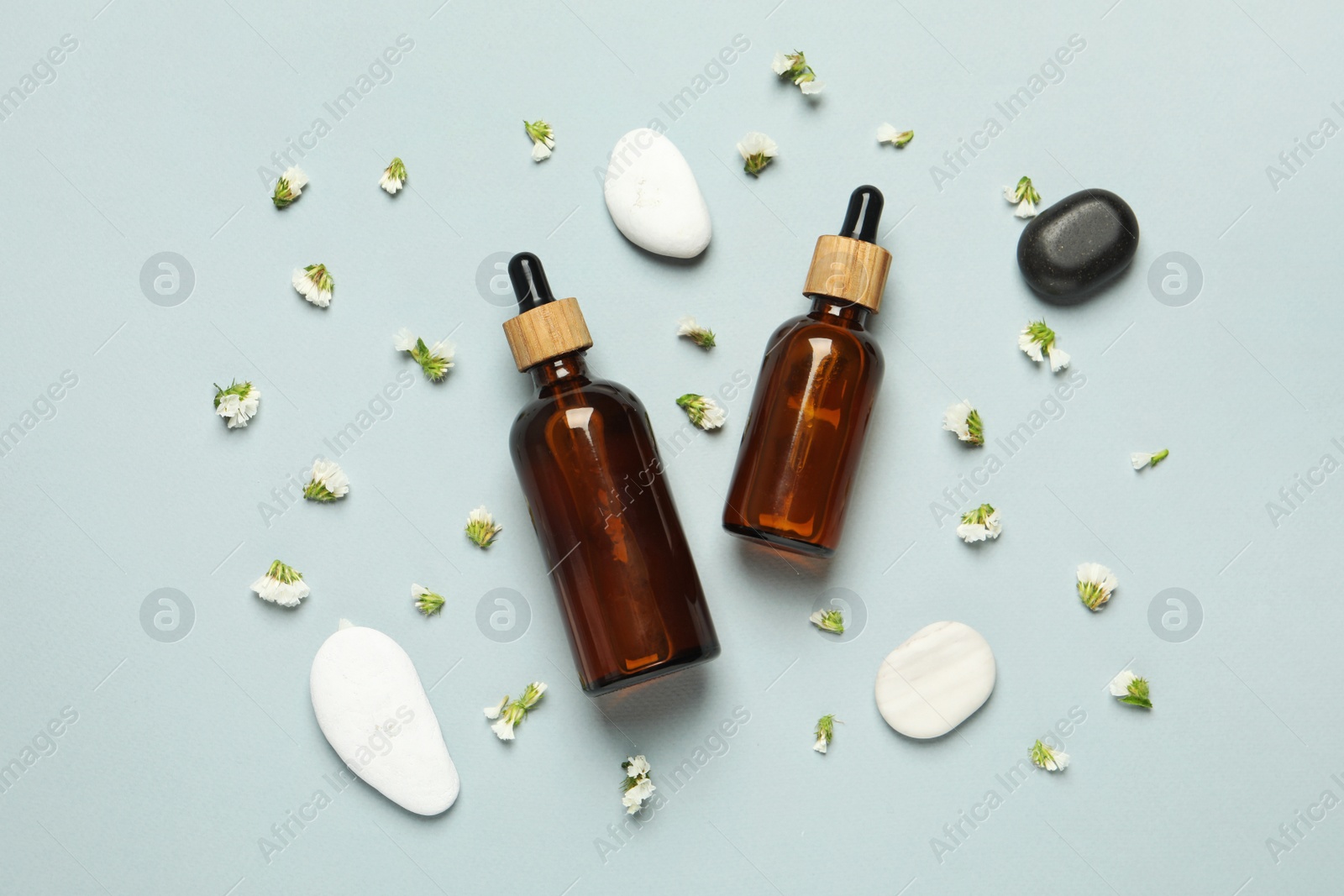 Photo of Flat lay composition with bottles of face serum, spa stones and beautiful flowers on light grey background