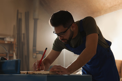 Photo of Professional carpenter making mark on wooden board in workshop