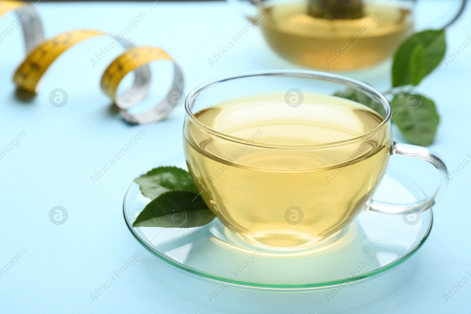 Photo of Glass cup of diet herbal tea and green leaves on light blue background