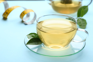 Photo of Glass cup of diet herbal tea and green leaves on light blue background