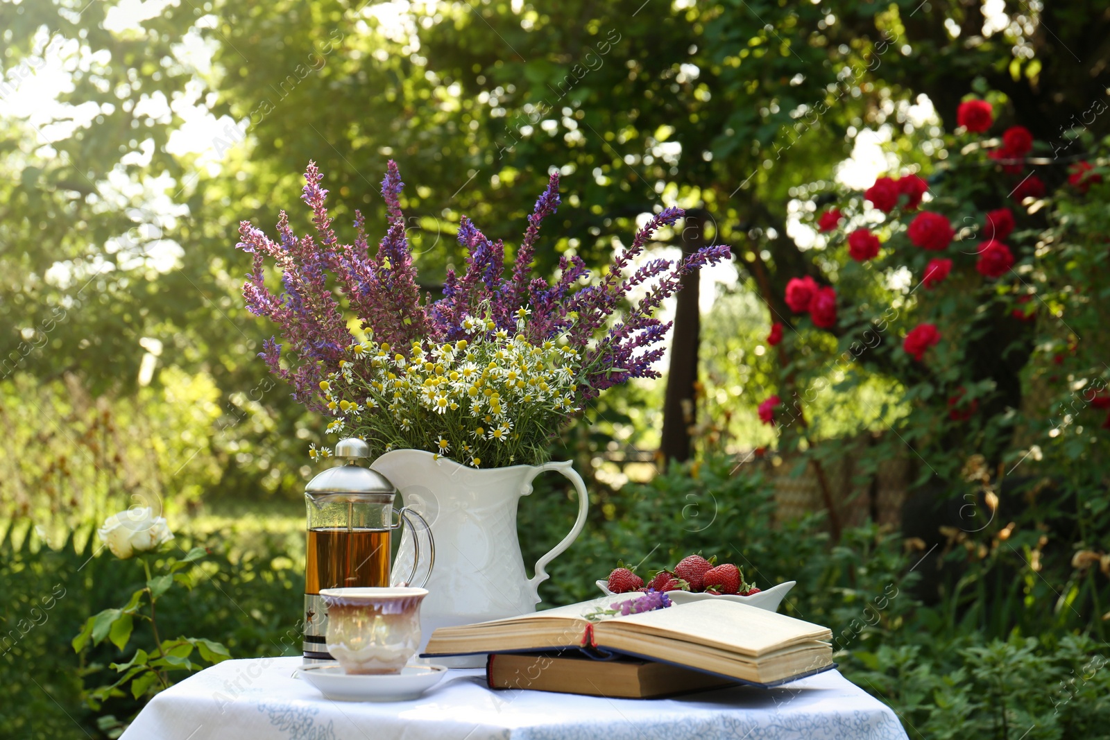 Photo of Beautiful bouquet of wildflowers and books on table served for tea drinking in garden