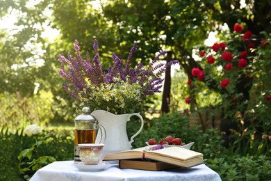 Beautiful bouquet of wildflowers and books on table served for tea drinking in garden