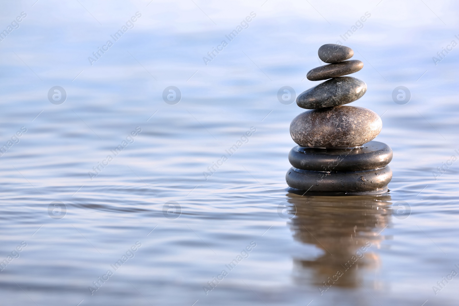 Photo of Stack of dark stones in sea water, space for text. Zen concept