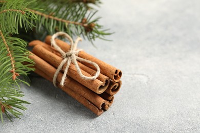 Photo of Bunch of cinnamon sticks and fir branches on grey textured table, closeup. Space for text