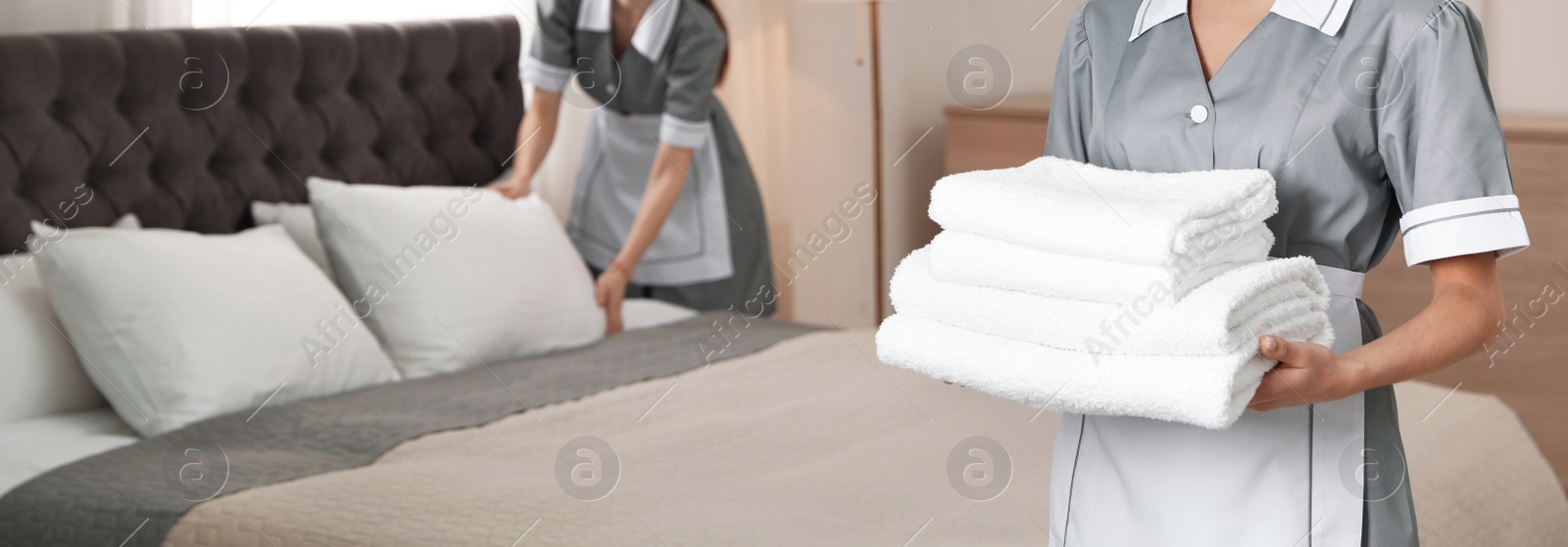 Image of Chambermaid holding stack of fresh towels in hotel room, closeup view with space for text. Banner design