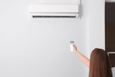 Photo of Woman operating air conditioner with remote control indoors