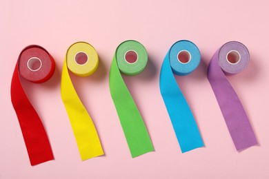 Bright kinesio tape in rolls on pink background, flat lay