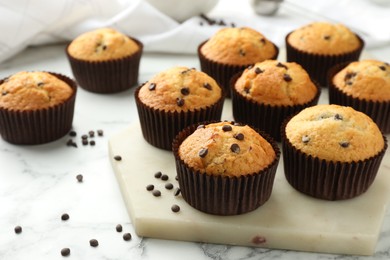 Photo of Delicious sweet muffins with chocolate chips on white marble table, space for text