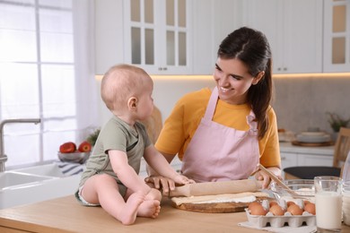 Happy young woman and her cute baby cooking together in kitchen