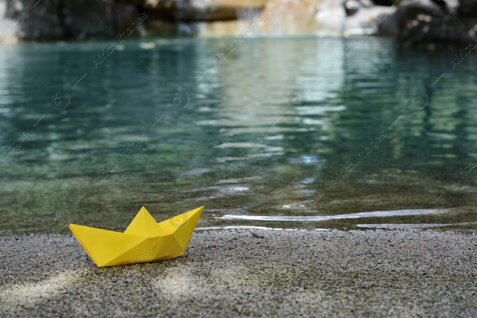 Photo of Beautiful yellow paper boat on sandy beach near pond, space for text