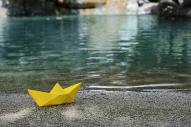 Beautiful yellow paper boat on sandy beach near pond, space for text