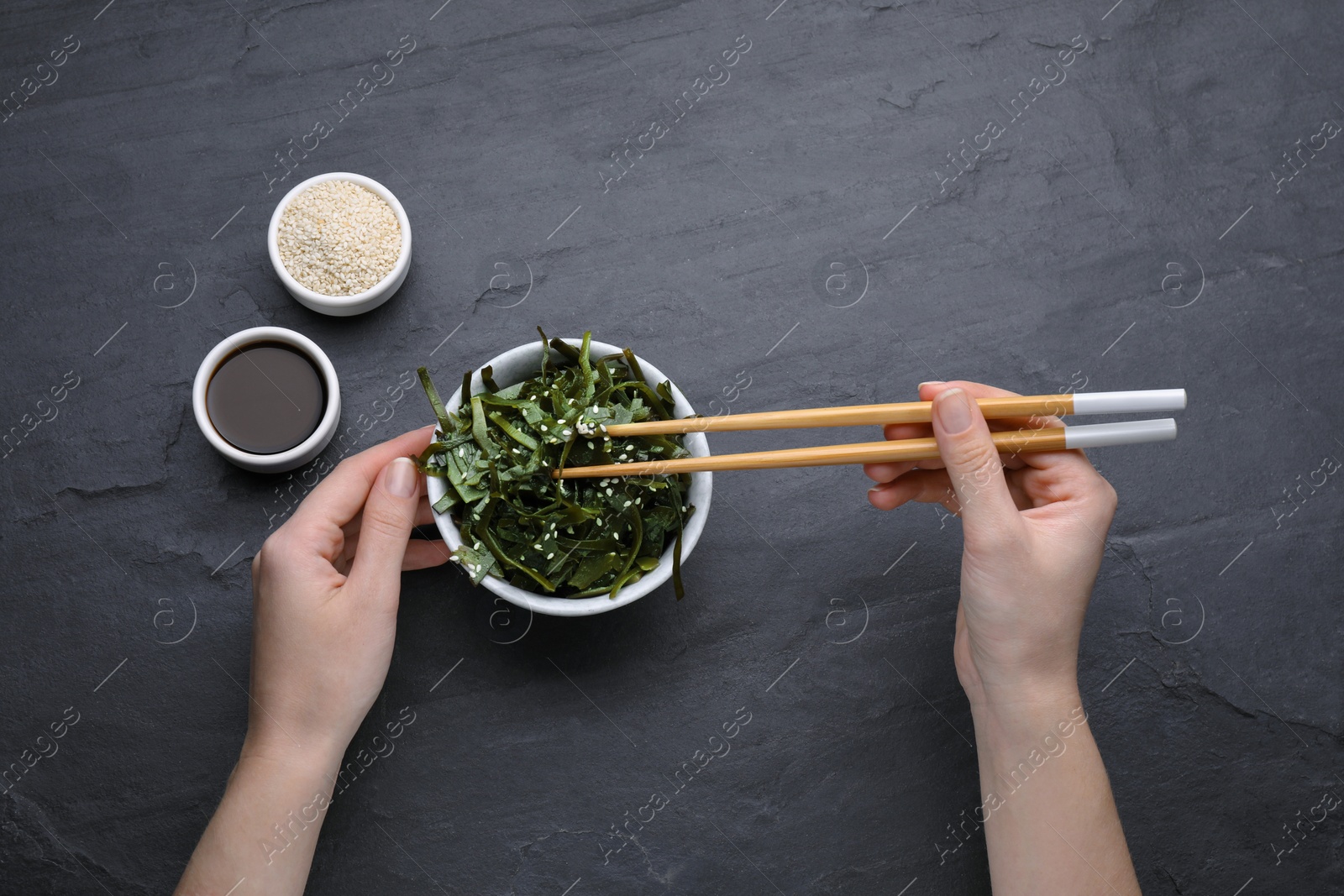 Photo of Woman eating fresh laminaria (kelp) seaweed at black table, top view