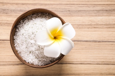 White sea salt for spa scrubbing procedure and flower on wooden background, top view