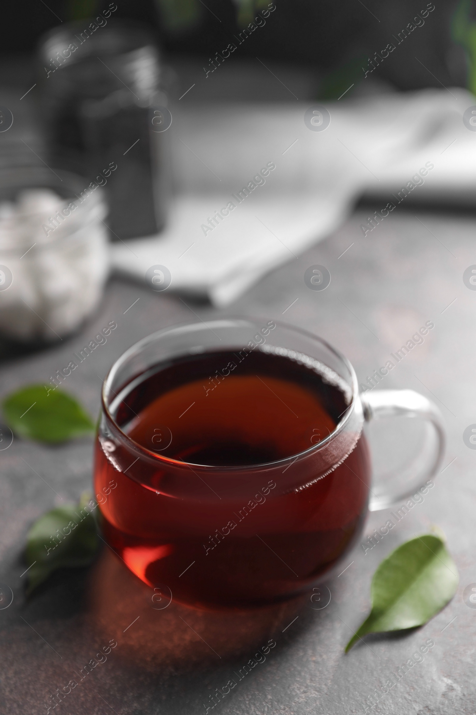 Photo of Tasty hot tea in cup and leaves on grey table, closeup