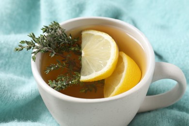 Photo of Cup of tasty herbal tea with thyme and lemon on turquoise fabric, closeup