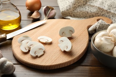 Photo of Cutting board with mushrooms and knife on wooden table, closeup