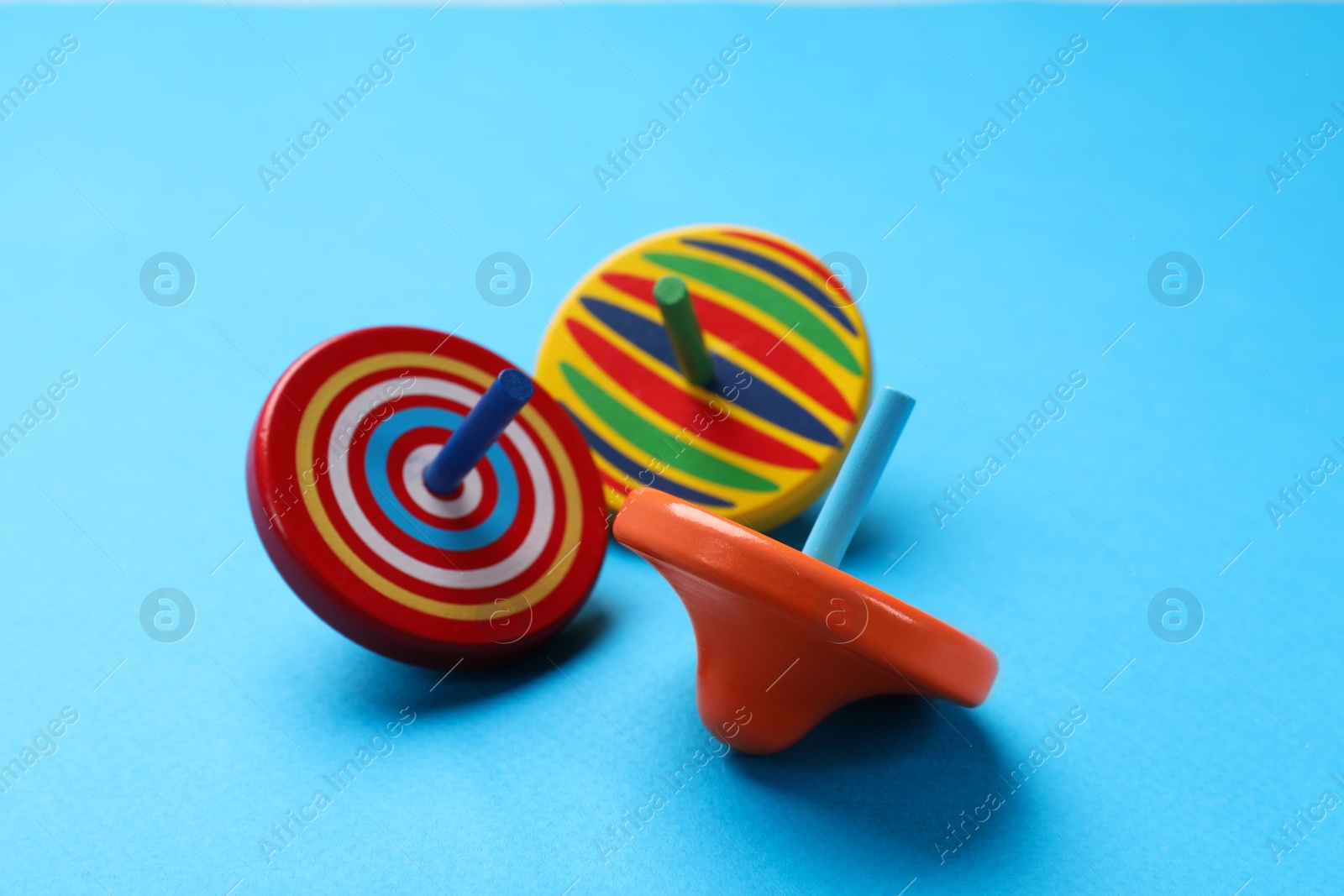 Photo of Many colorful spinning tops on light blue background, closeup