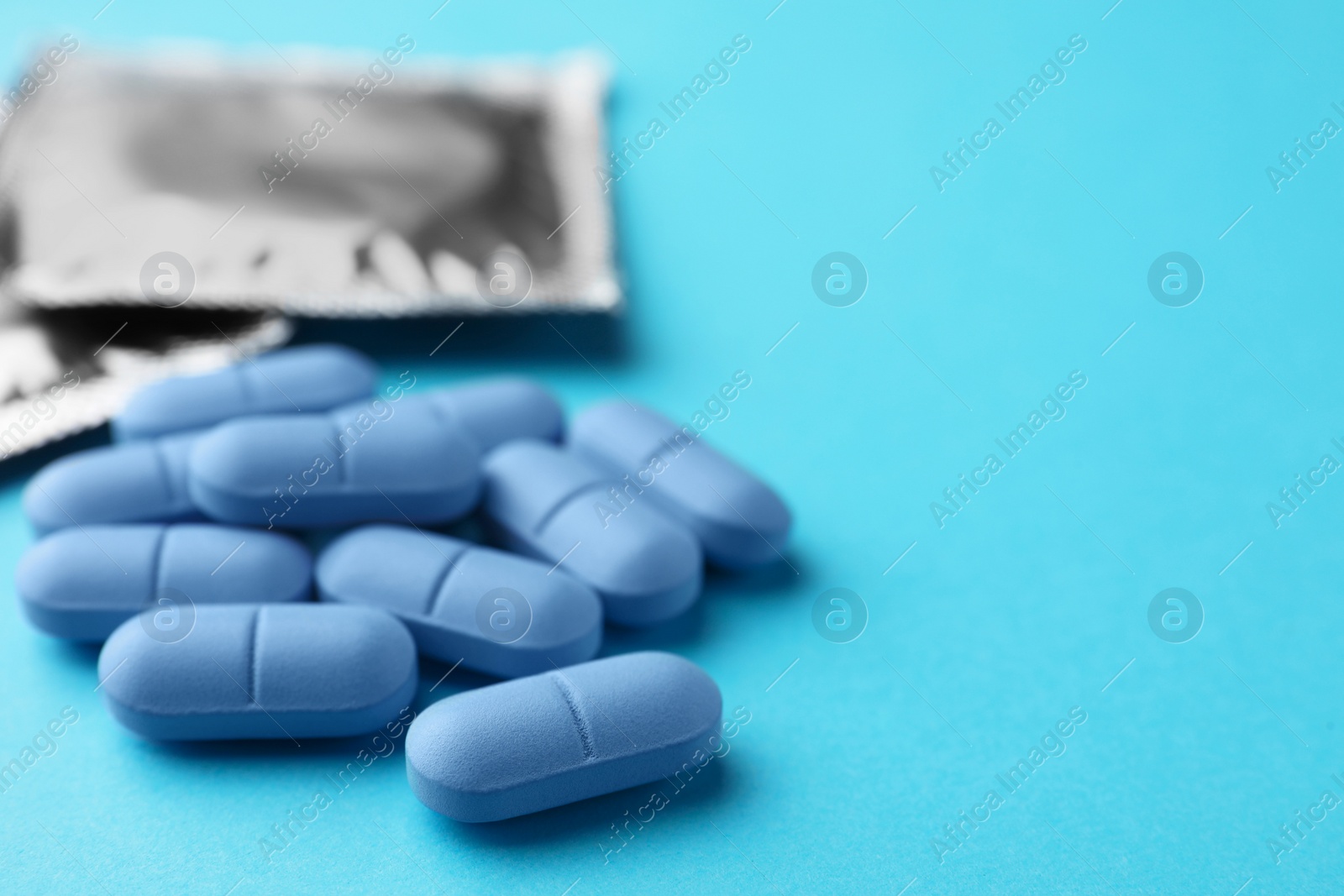 Photo of Pills and condoms on light blue background, space for text. Potency problem