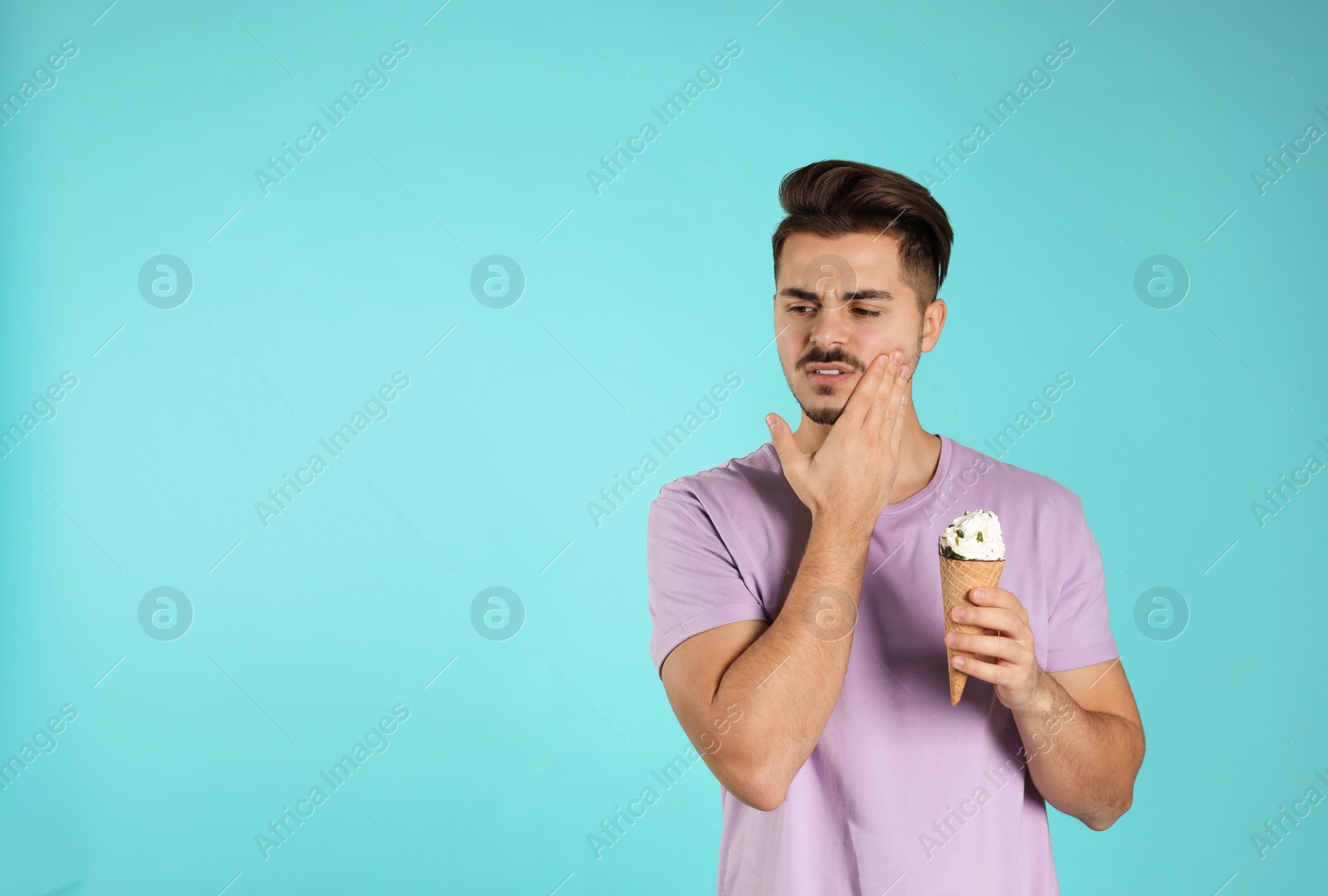 Photo of Emotional young man with sensitive teeth and ice cream on color background. Space for text