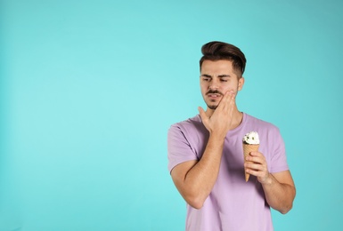 Emotional young man with sensitive teeth and ice cream on color background. Space for text