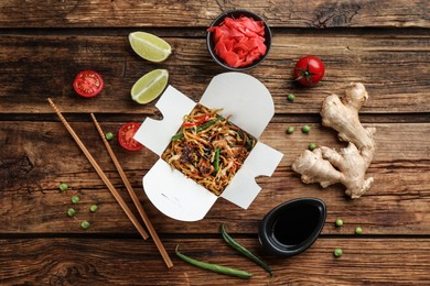 Photo of Box of wok noodles with vegetables and meat on wooden table, flat lay