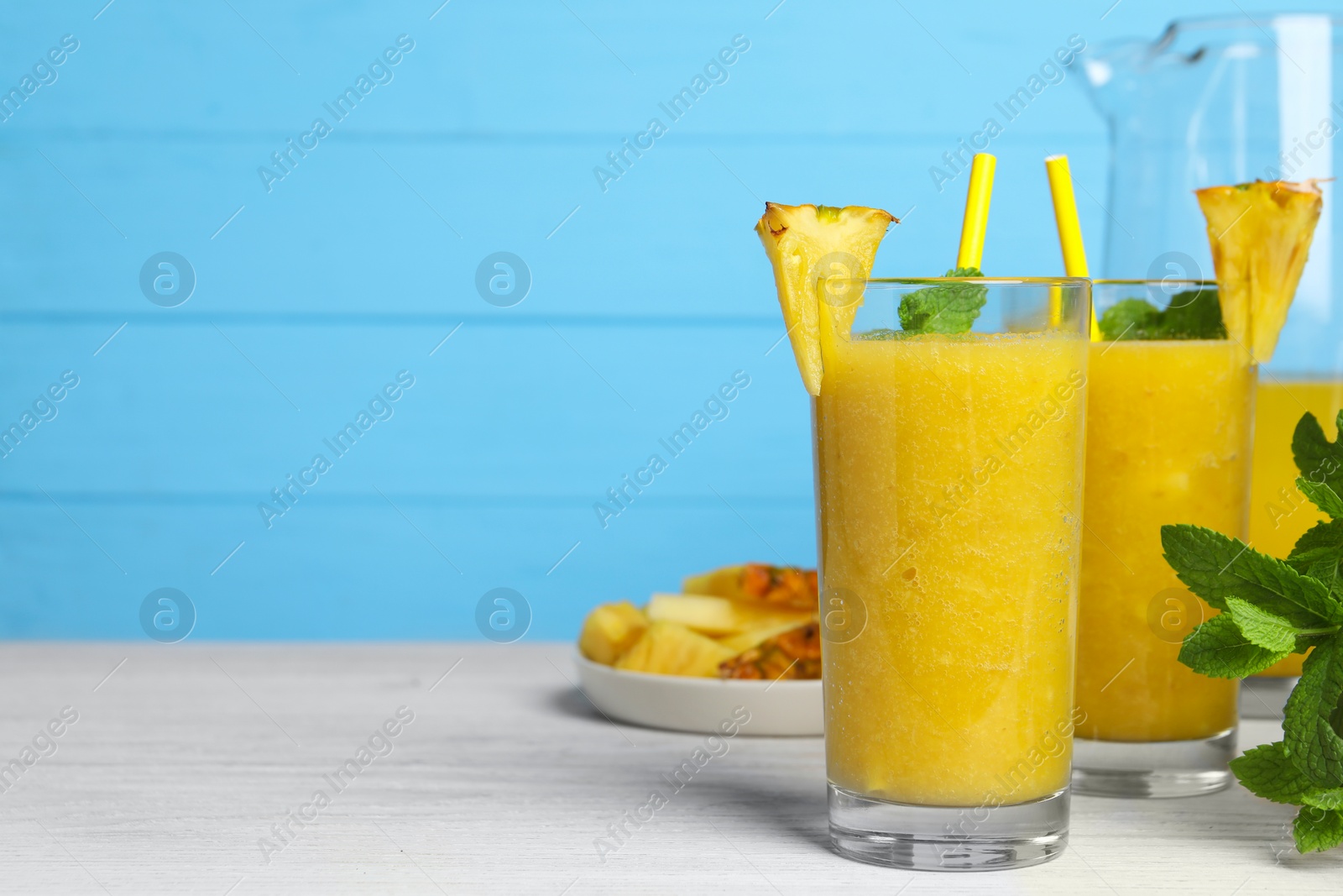 Photo of Tasty pineapple smoothie, mint and cut fruit on white wooden table, space for text