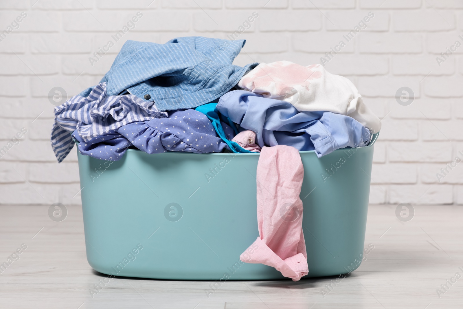 Photo of Laundry basket with clothes near white brick wall