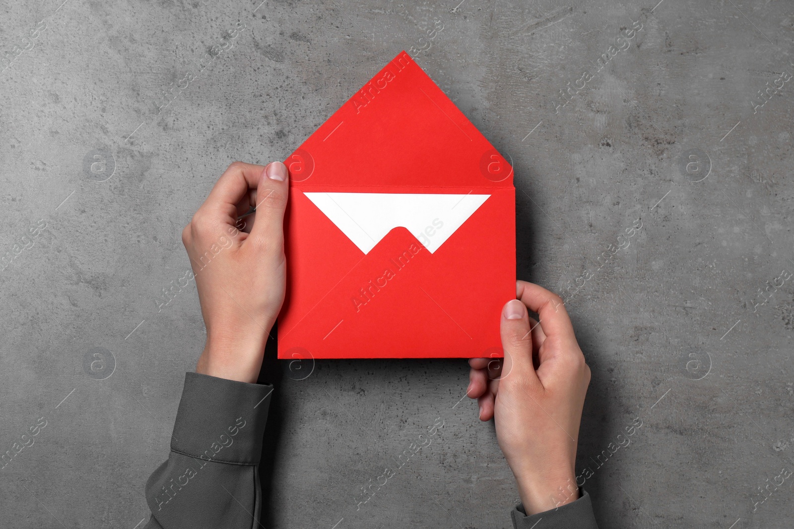 Photo of Woman holding letter envelope with card at grey textured table, top view