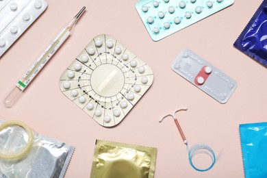 Photo of Contraceptive pills, condoms, intrauterine device and thermometer on beige background, flat lay. Different birth control methods