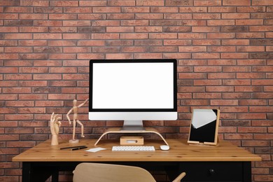 Photo of Modern computer and tablet with blank screens on desk near brick wall, space for design. Comfortable workplace
