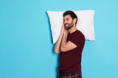 Photo of Sleepy handsome man with pillow on light blue background, space for text