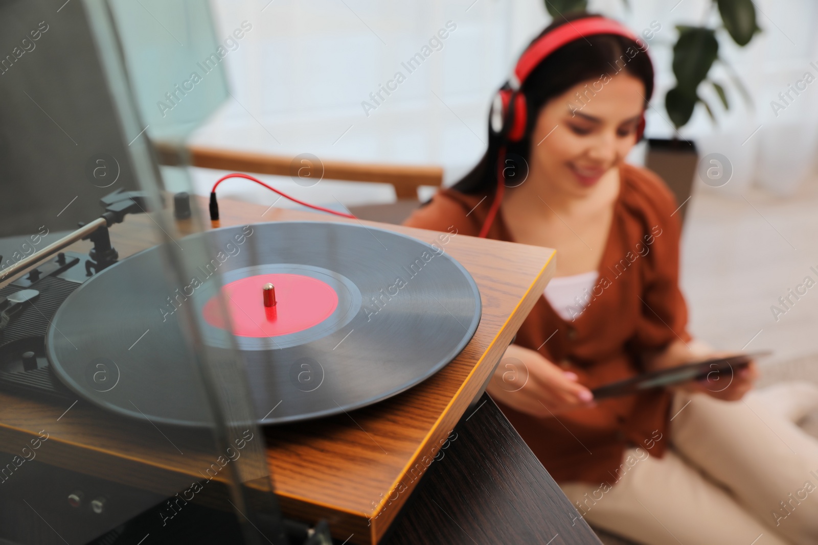 Photo of Woman listening to music at home, focus on turntable
