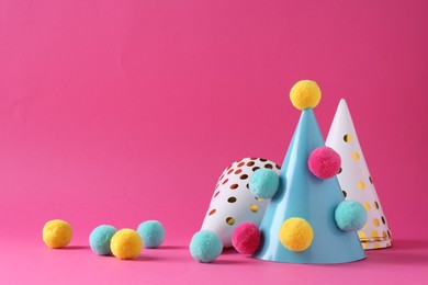 Photo of Party hats with color pompoms on pink background