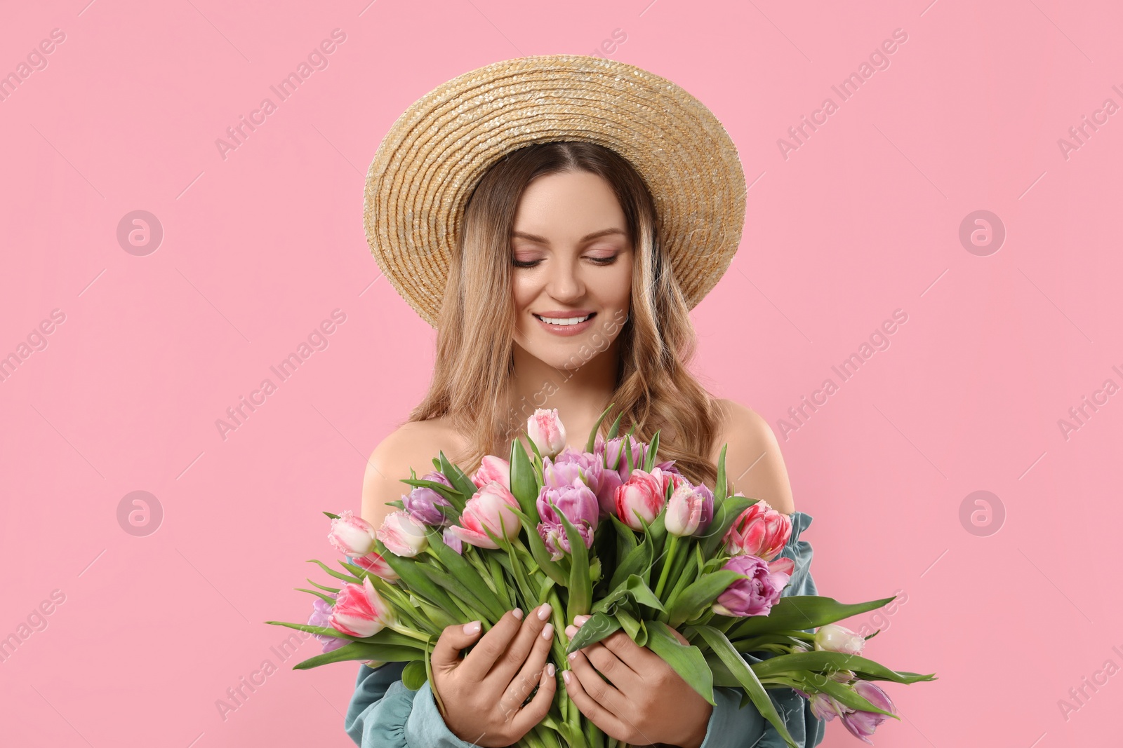 Photo of Happy young woman in straw hat holding bouquet of beautiful tulips on pink background