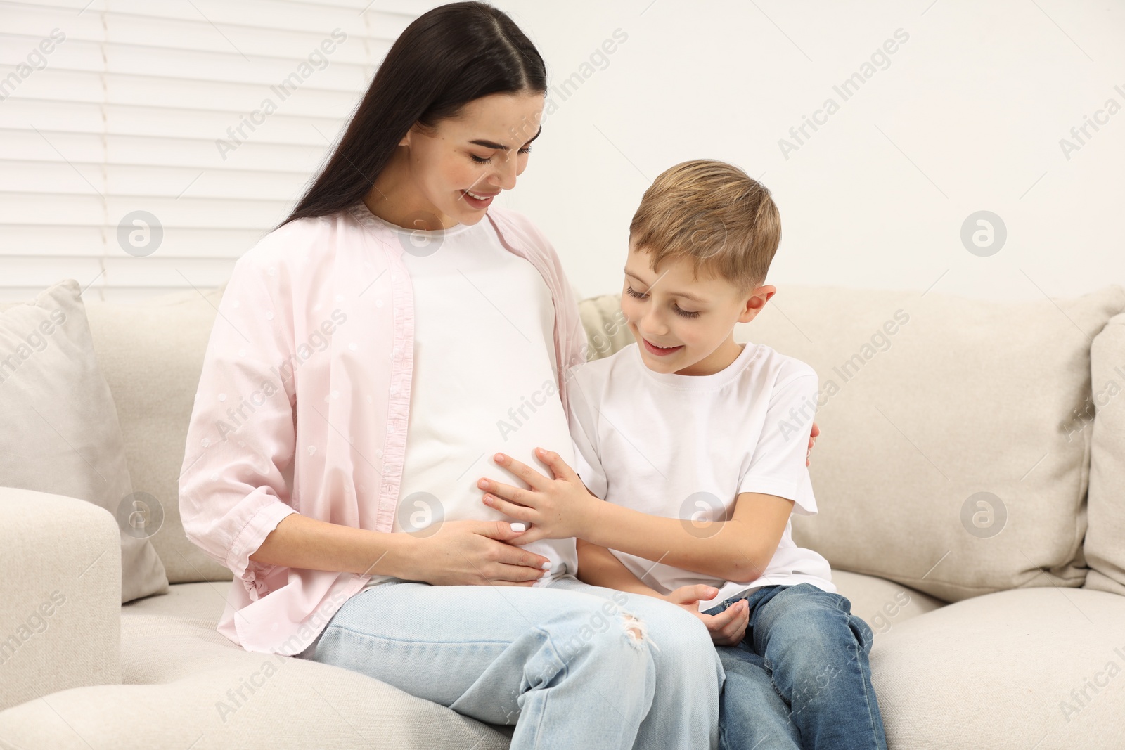 Photo of Cute boy touching pregnant mother's belly at home