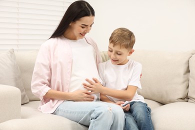 Cute boy touching pregnant mother's belly at home