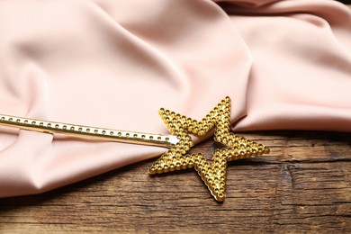 Photo of Beautiful golden magic wand and pink fabric on wooden table, closeup