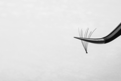 Photo of Tweezers with bunch of artificial eyelashes on white background, closeup. Space for text
