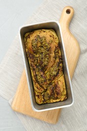 Freshly baked pesto bread in loaf pan on light table, top view