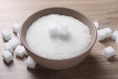 Different types of white sugar in bowl on wooden table, closeup