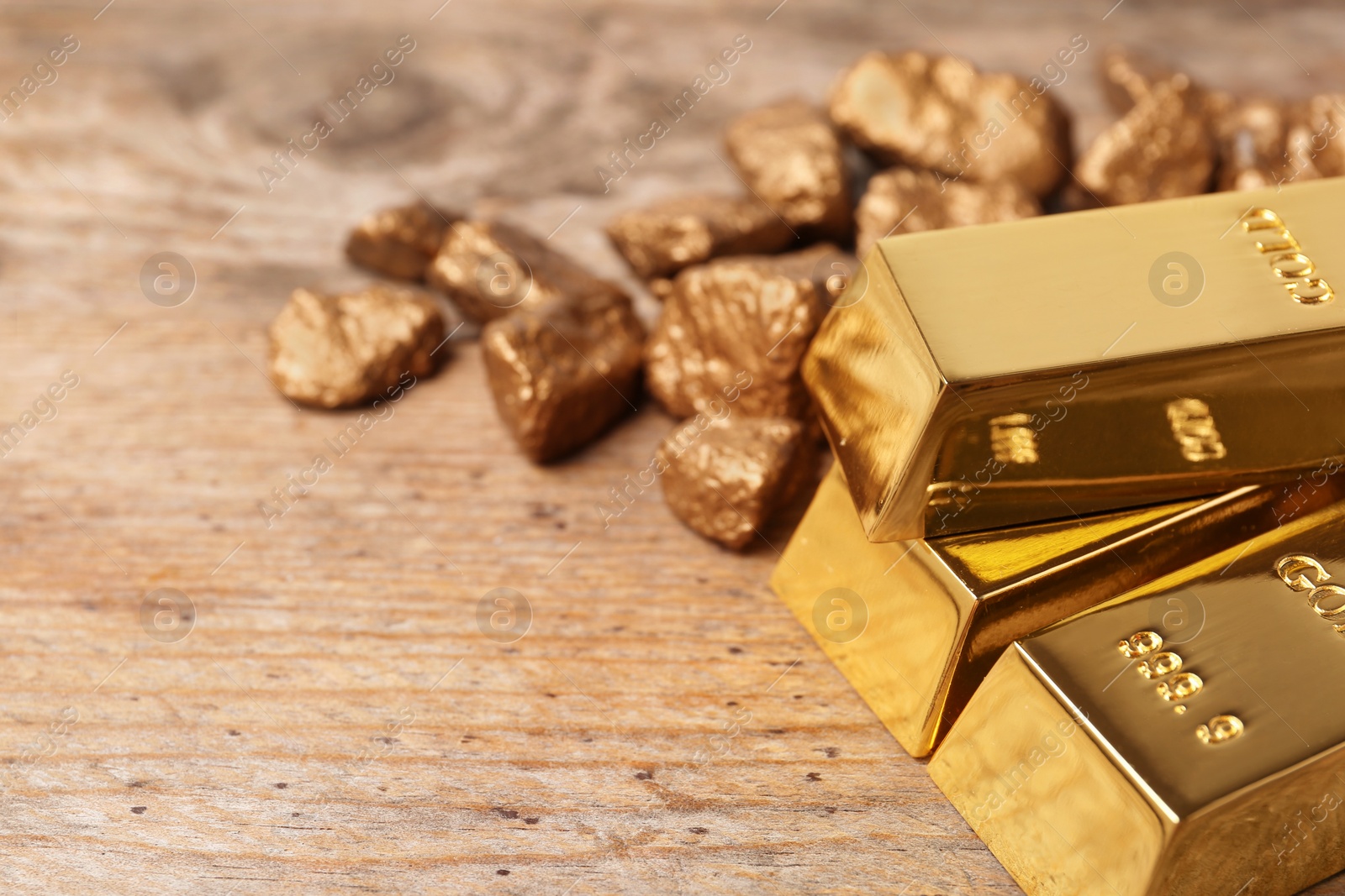 Photo of Gold nuggets and ingots on wooden background. Space for text