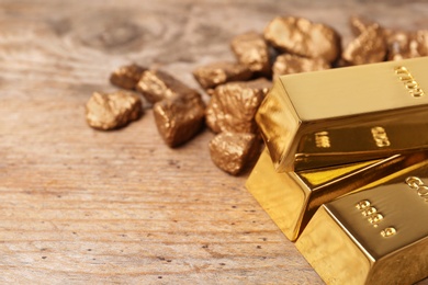 Gold nuggets and ingots on wooden background. Space for text