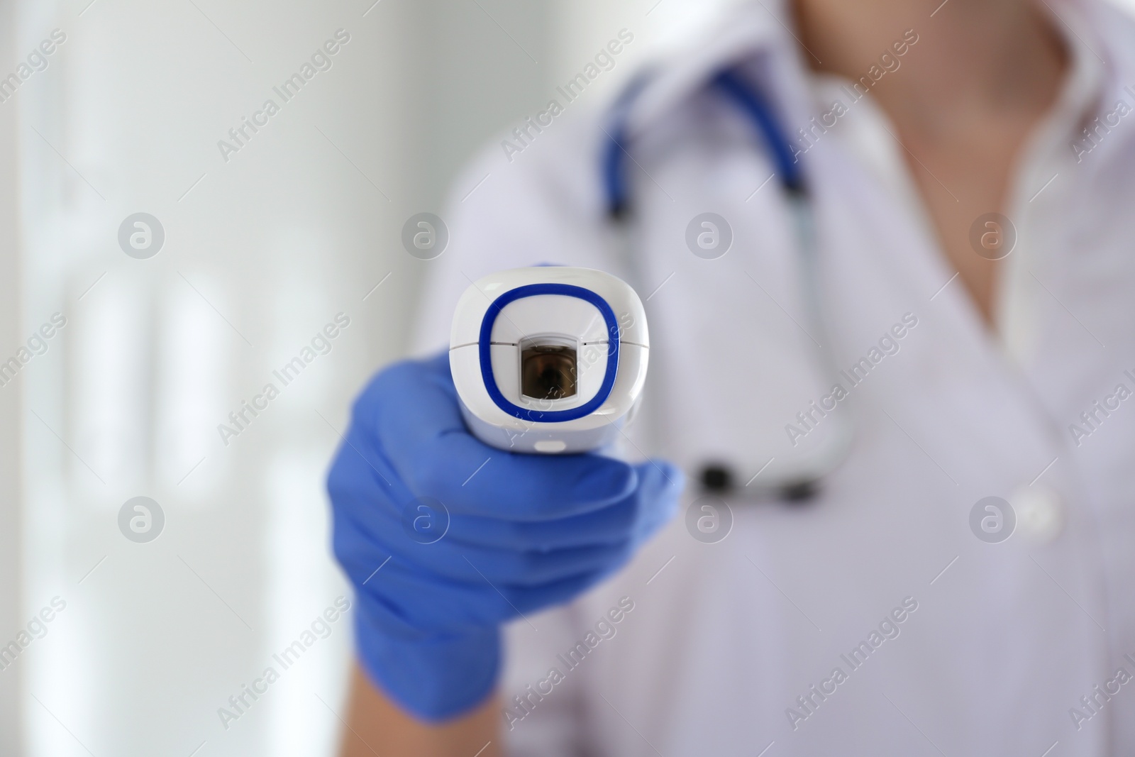 Photo of Doctor holding non contact infrared thermometer indoors, focus on hand. Measuring temperature