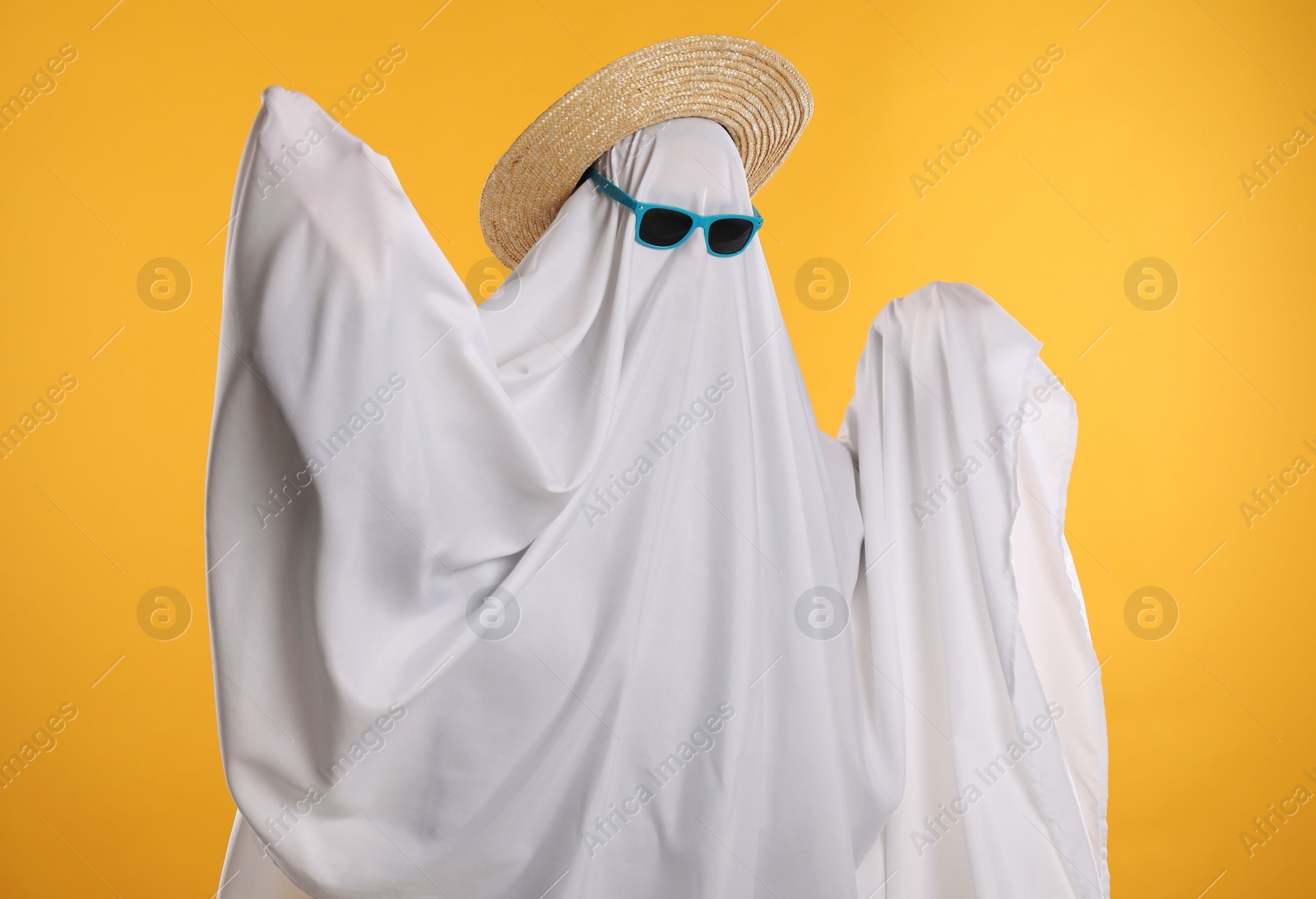 Photo of Person in ghost costume, sunglasses and straw hat on yellow background