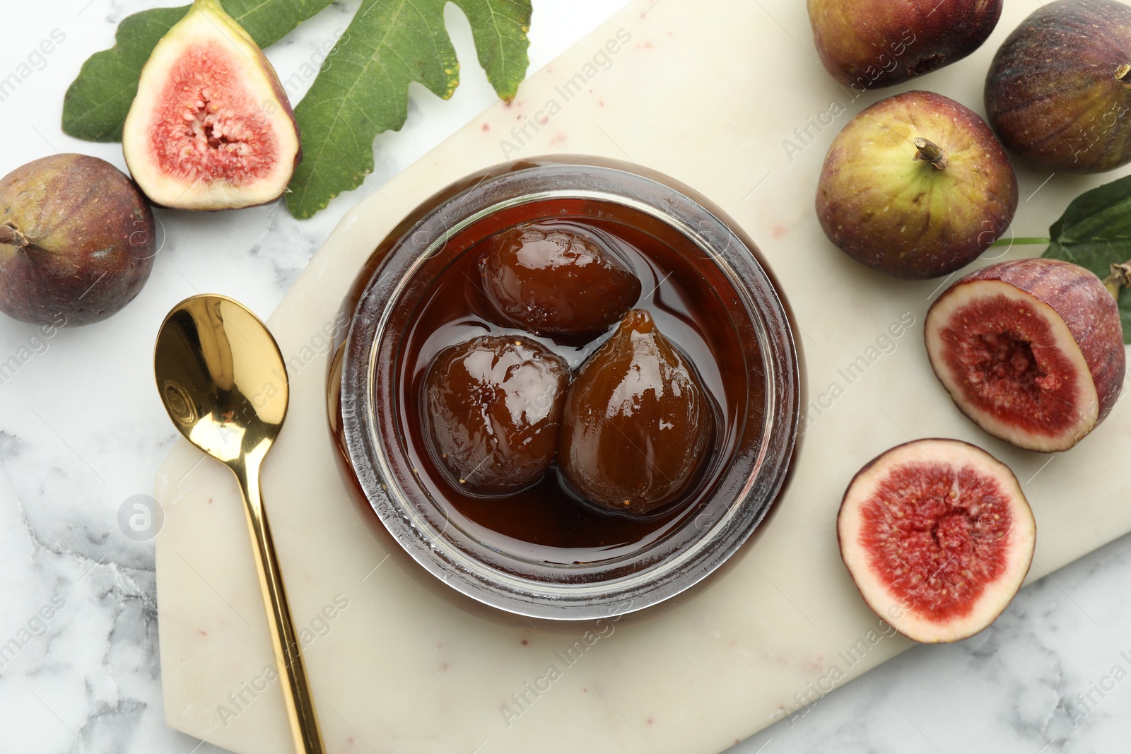 Photo of Jar of tasty sweet jam and fresh figs on white marble table, flat lay