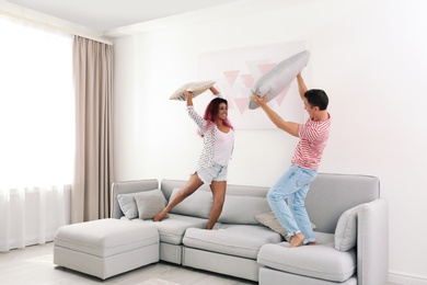 Happy couple having pillow fight on sofa at home