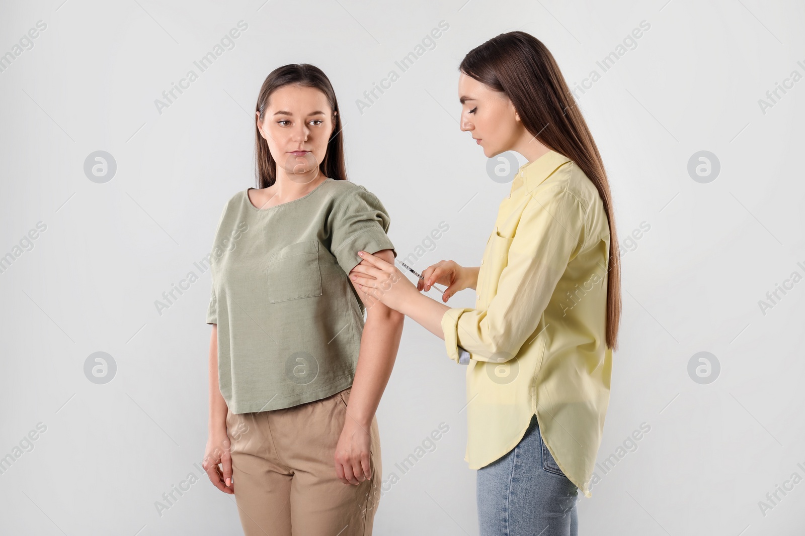 Photo of Woman giving insulin injection to her diabetic friend on grey background