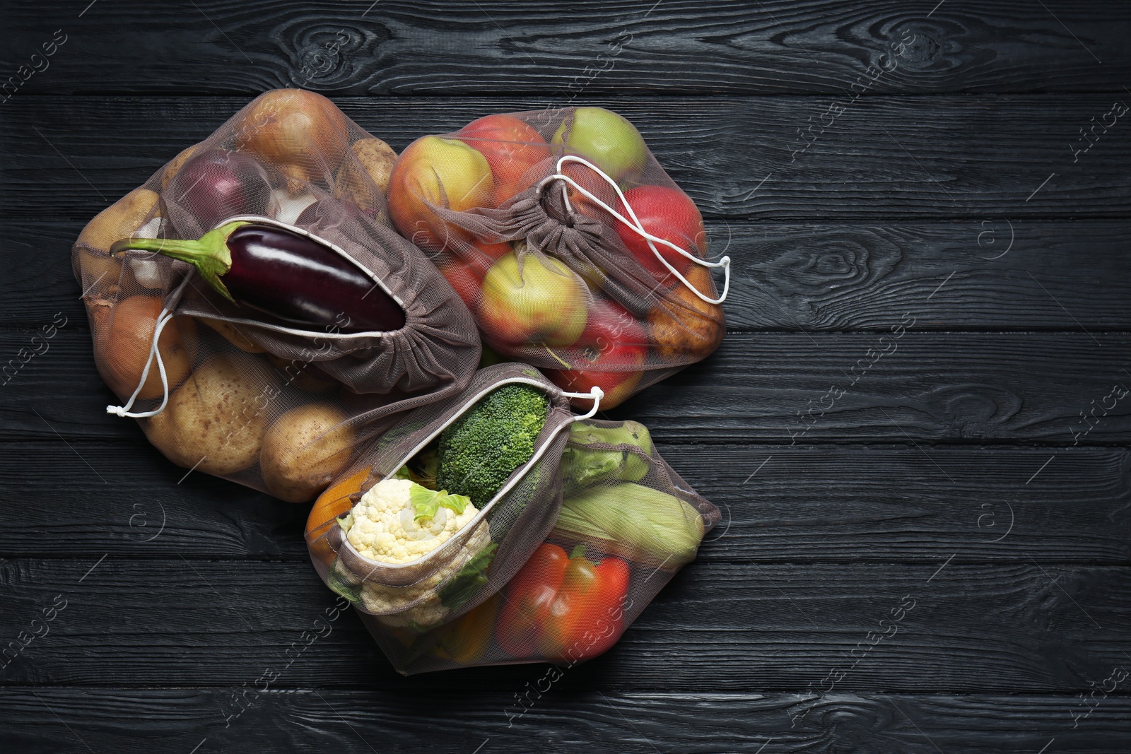 Photo of Different fresh vegetables in bags on black wooden table, flat lay and space for text. Farmer harvesting